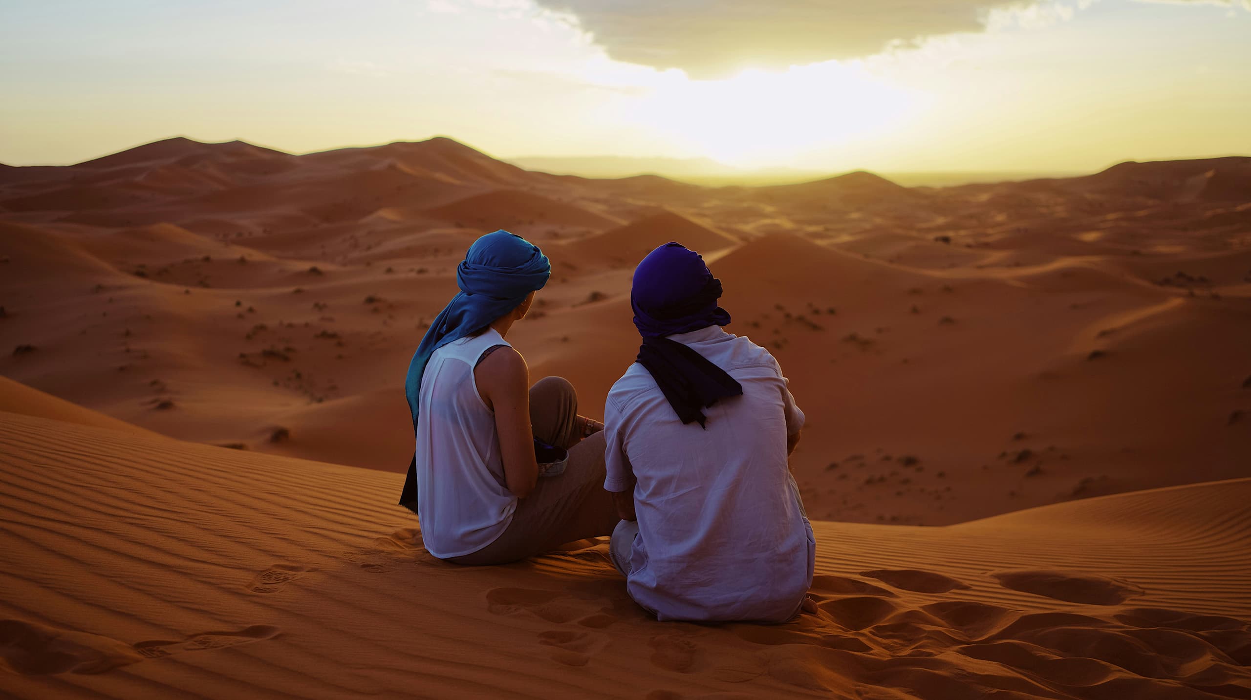 ein Pärrchen von Touristen mit Turban sitzen auf einem Sandberg und genießen die Aussicht 